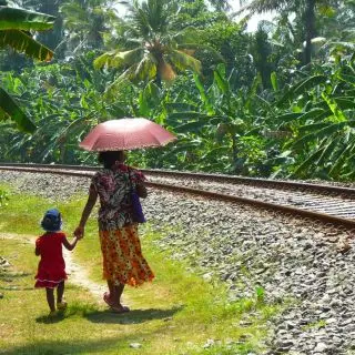 Maminka s dcerkou jdou nakoupit do vedlejší vesnice podél kolejí. Deštníkem se chrání před silným tropickým